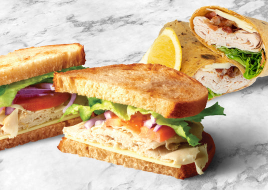 photo of a lunch turkey sandwiches and turkey bacon wrap with lemon on wedge on marble.