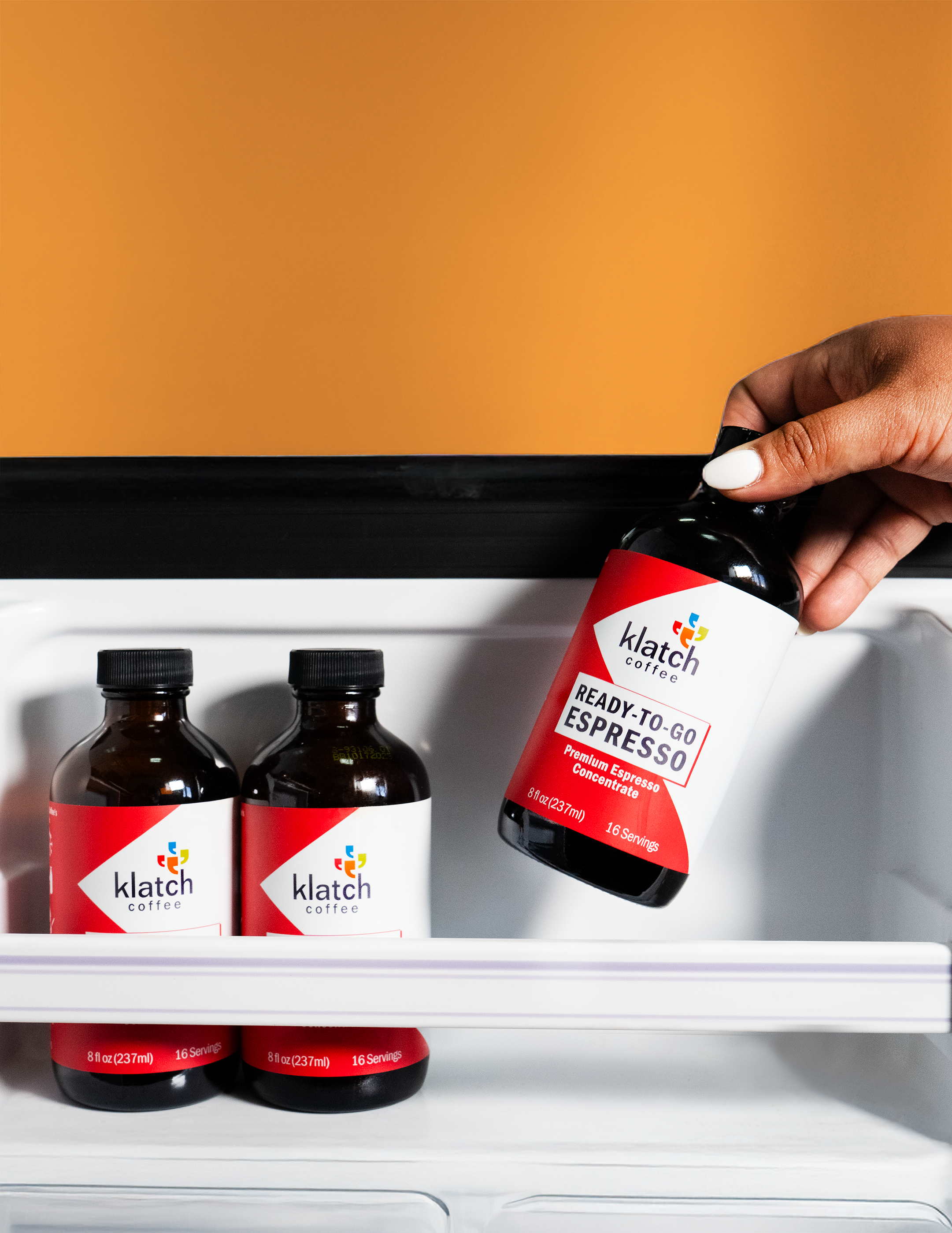 Hand grabbing an 8oz bottle of ready to go espresso out of a fridge next to two espresso bottles.