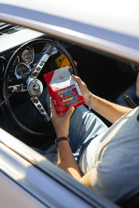 Person sitting in a car holding a red Centennial coffee bag over stirring wheel.