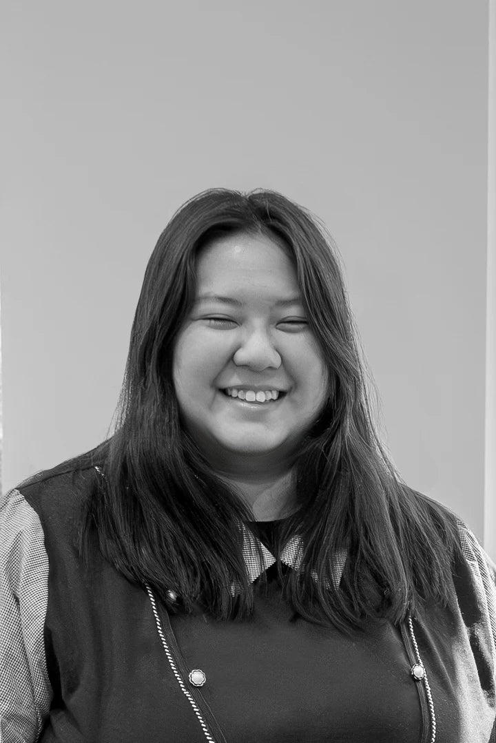 Black and white picture of a woman smiling at the camera in front of a white wall. 