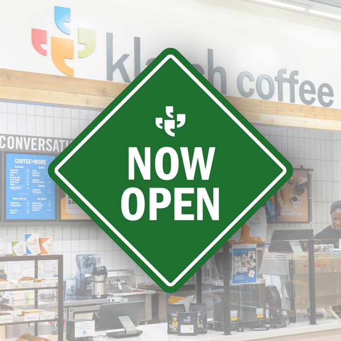A green diamond-shaped vector sign with the Klatch Coffee logo at the top and “Now Open” beneath it, placed over a photo of a Klatch Coffee cafe. 