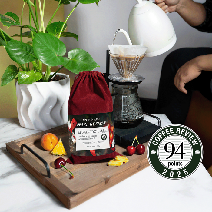 El Salvador Jasal Orange Red Velvet coffee bag on a tray surrounded by pineapple, cherries, and apricots.
