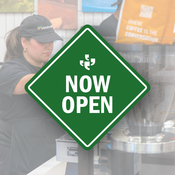 A green diamond-shaped vector sign with the Klatch Coffee logo at the top and “Now Open” beneath it, placed over a photo of a Klatch Coffee cafe. 