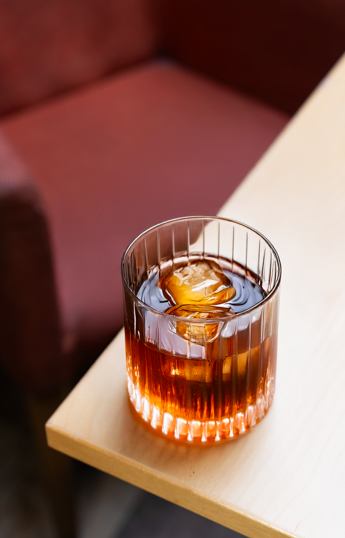 Glass of an espresso old fashioned on the edge of a table. 